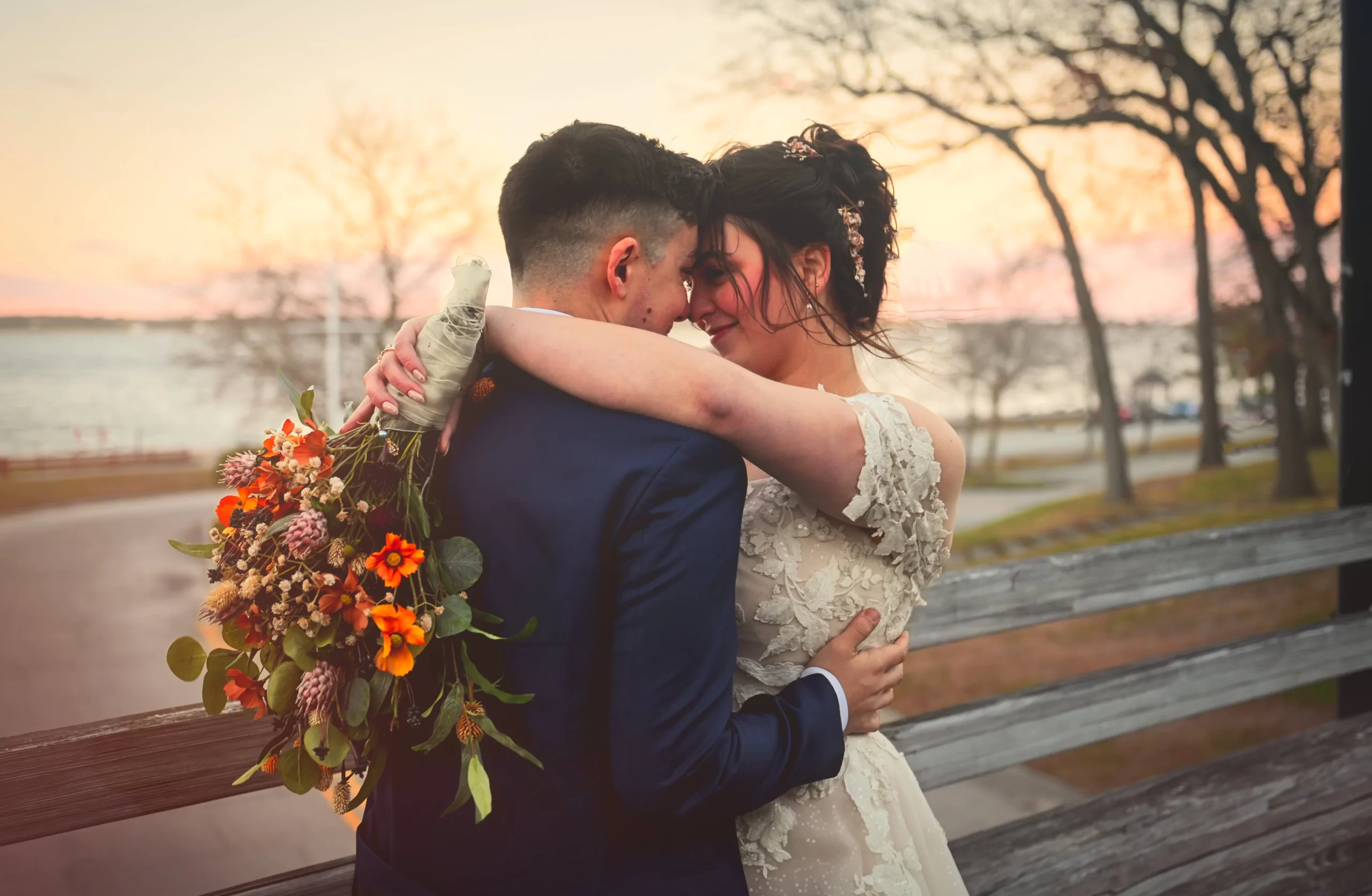Alex & Caleb embrace on bridge, ocean view in background.